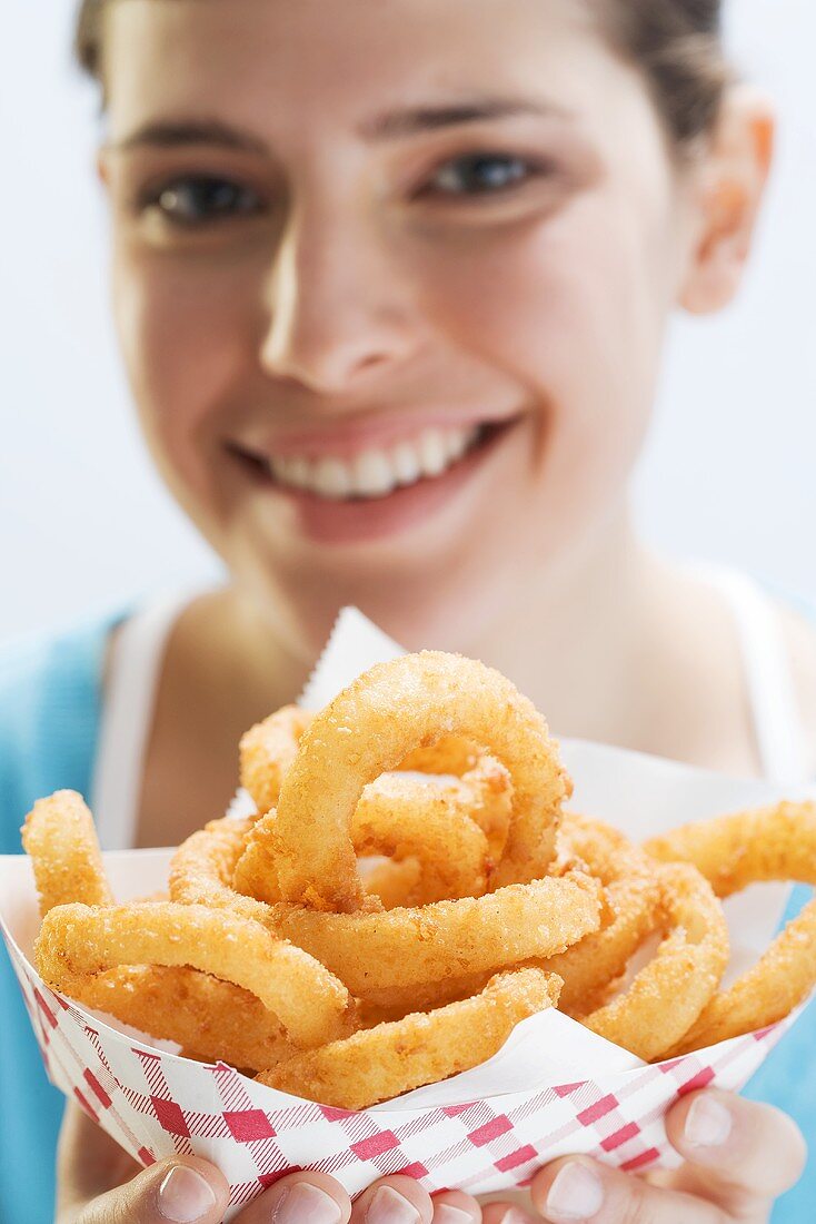 Young woman holding deep-fried onion rings in paper dish
