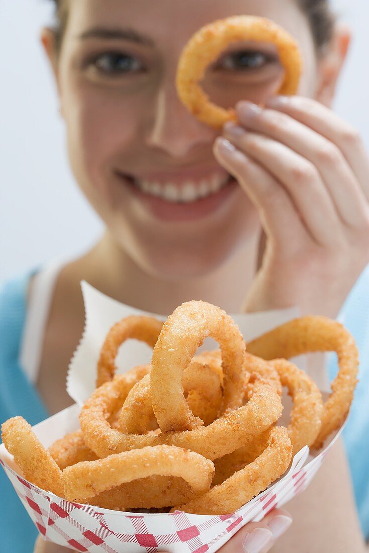 Young woman holding deep-fried onion rings in paper dish