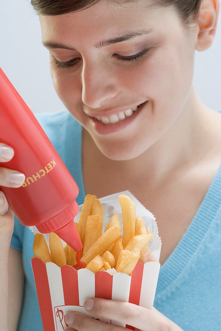 Junge Frau drückt Ketchup aus Flasche auf Pommes frites