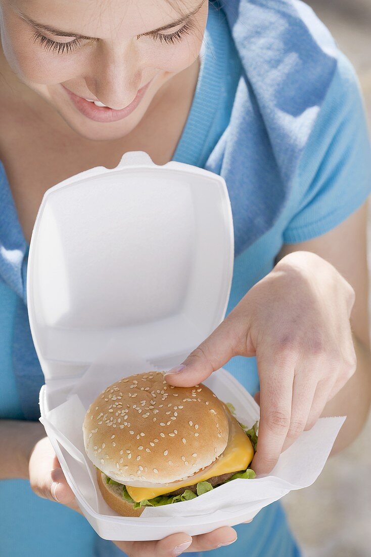 Young woman taking cheeseburger out of polystyrene box
