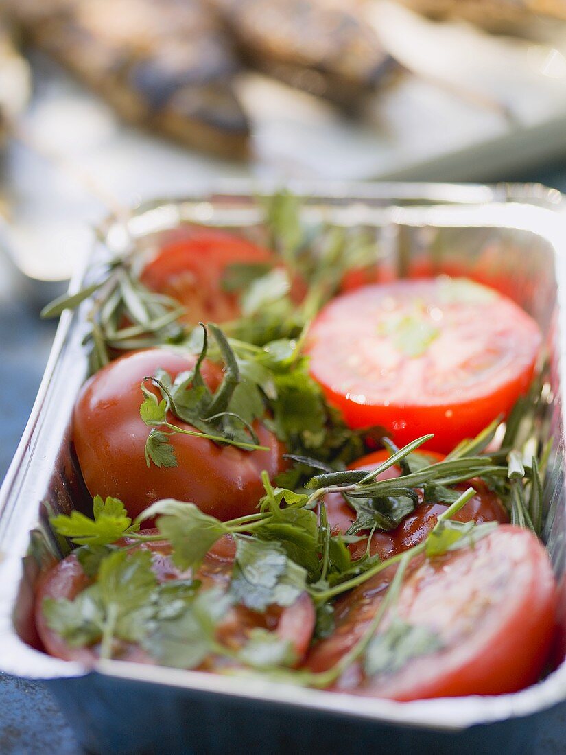Tomatoes with fresh herbs in aluminium dish, ready for grilling