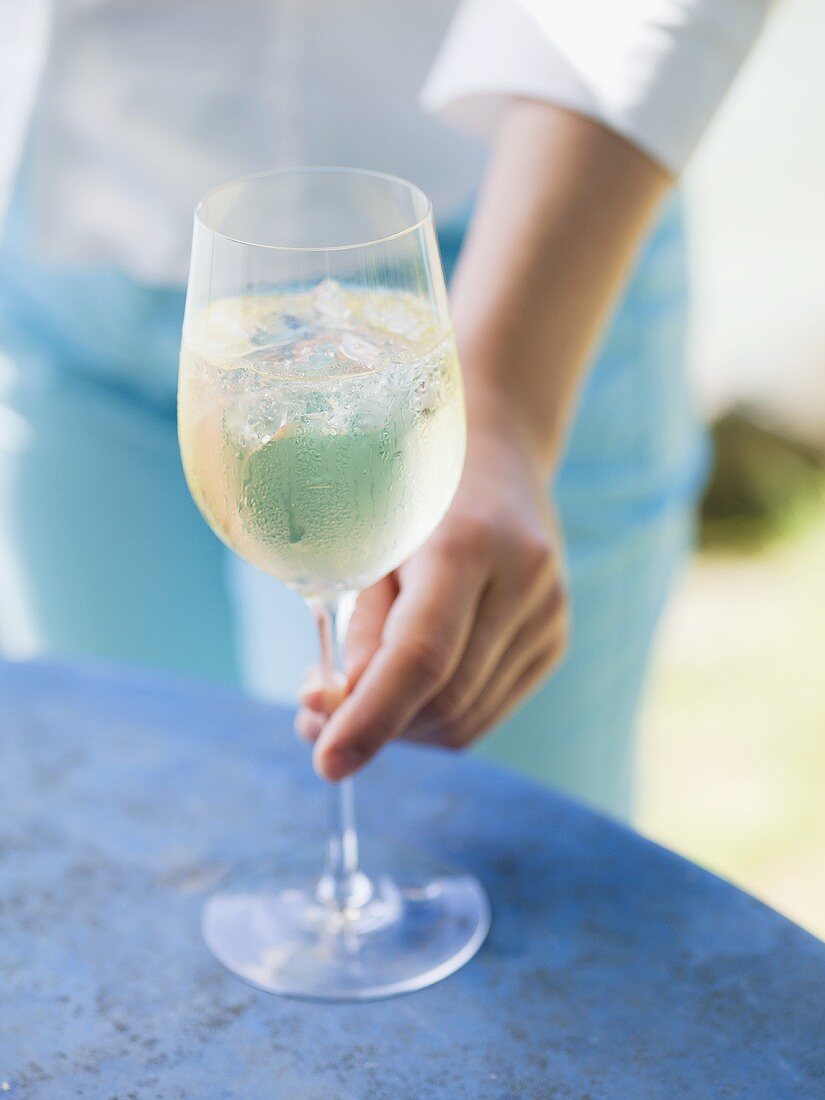 Woman reaching for glass of white wine with ice cubes on table