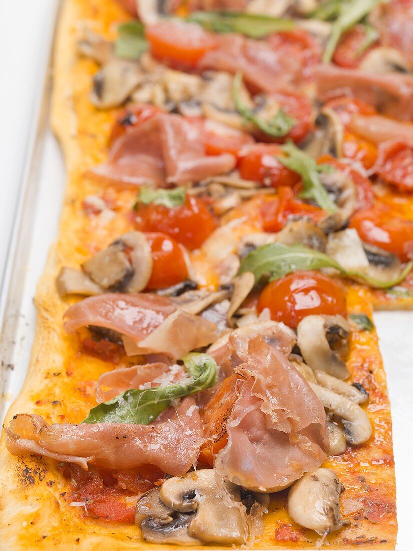 Pizza topped with ham, tomatoes, mushrooms and rocket