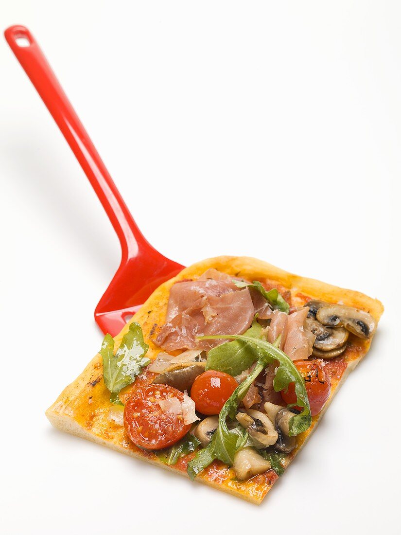 Slice of pizza topped with ham, tomatoes, mushrooms, rocket
