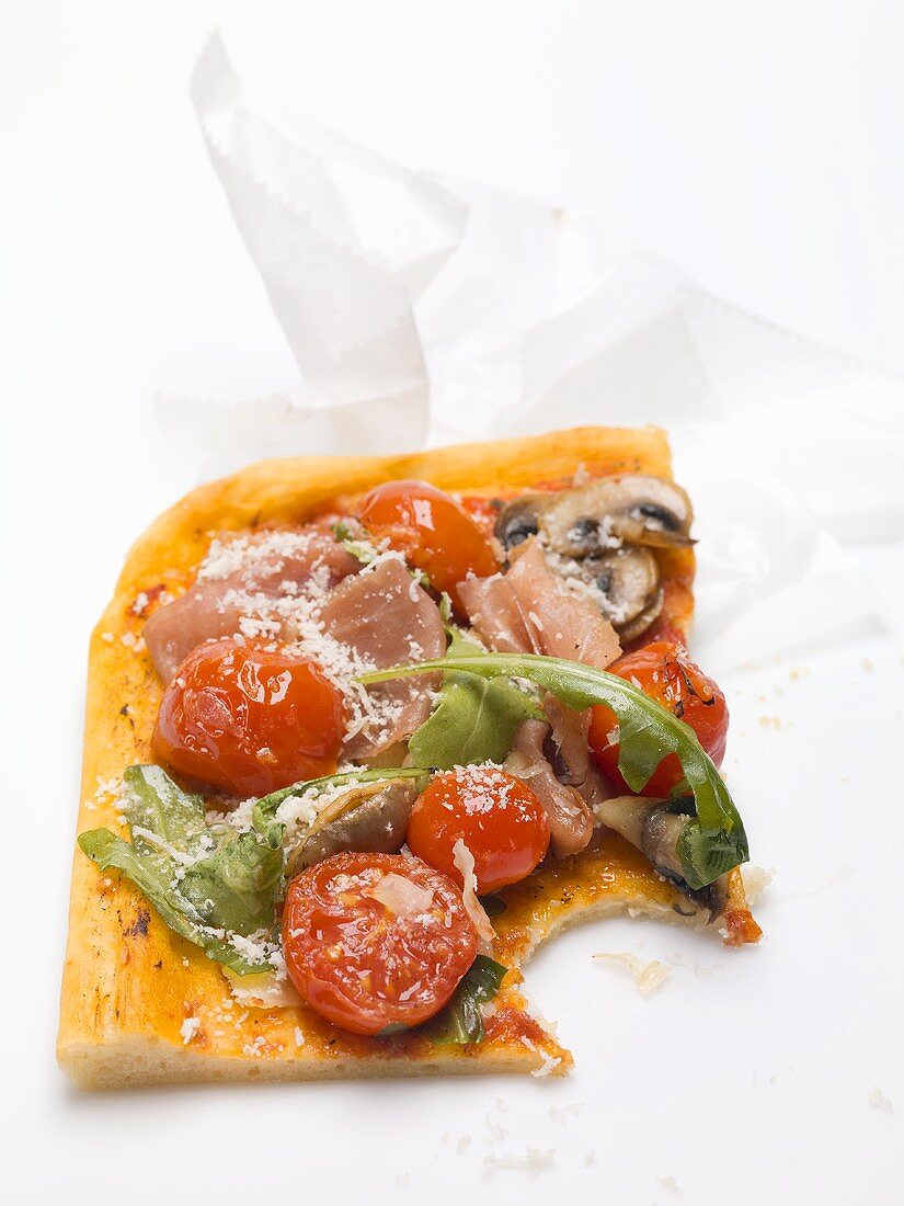 Pizzastück mit Schinken, Tomaten, Pilzen, Rucola (angebissen)