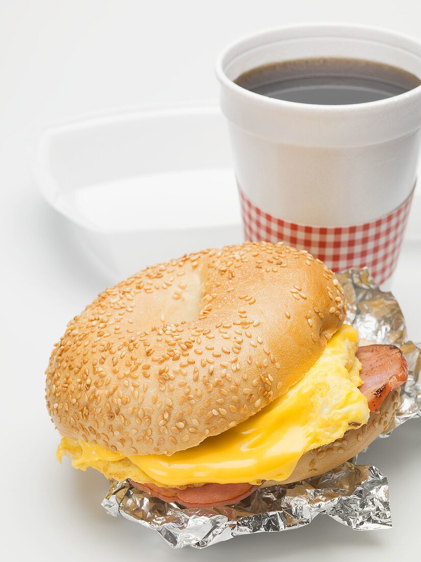 Sesame bagel with scrambled egg, cheese & ham, cup of coffee
