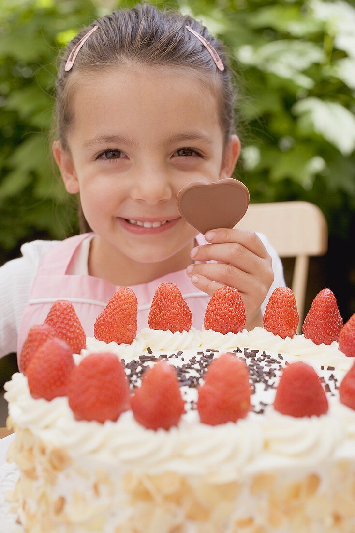 Little girl with chocolate heart behind large strawberry gateau