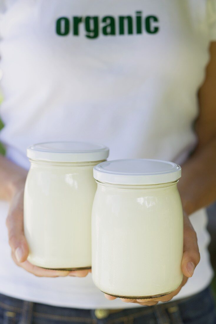 Hands holding two jars of organic yoghurt