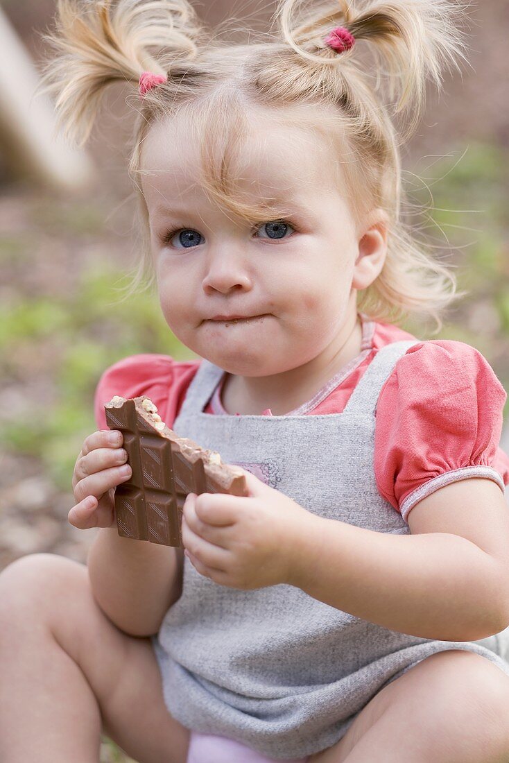 Little girl holding part of a bar of nut chocolate