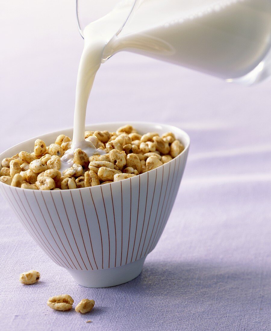 Pouring milk onto honey puffed wheat breakfast cereal