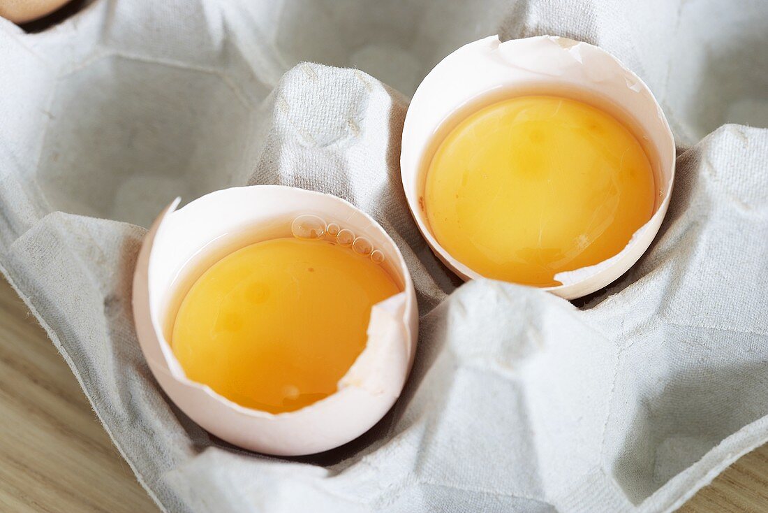 Two broken eggs in their shells in egg box