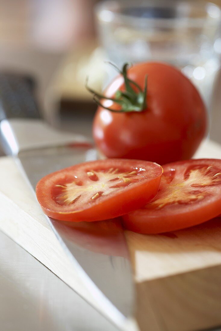 Whole tomato and tomato slices on chopping board