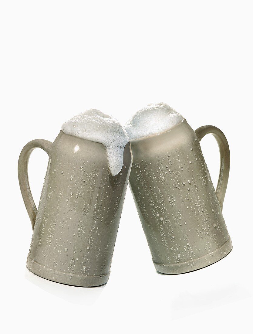 Two mugs of beer clinking together