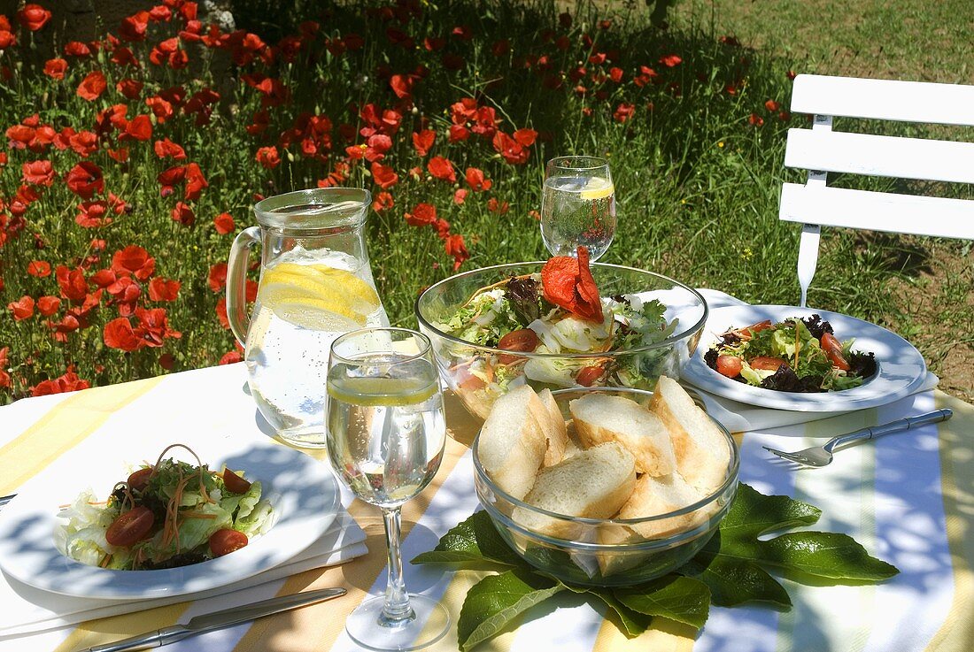 Gedeckter Tisch mit Salat und Brot im sommerlichen Garten