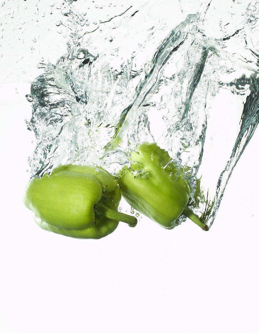 Two green peppers falling into water