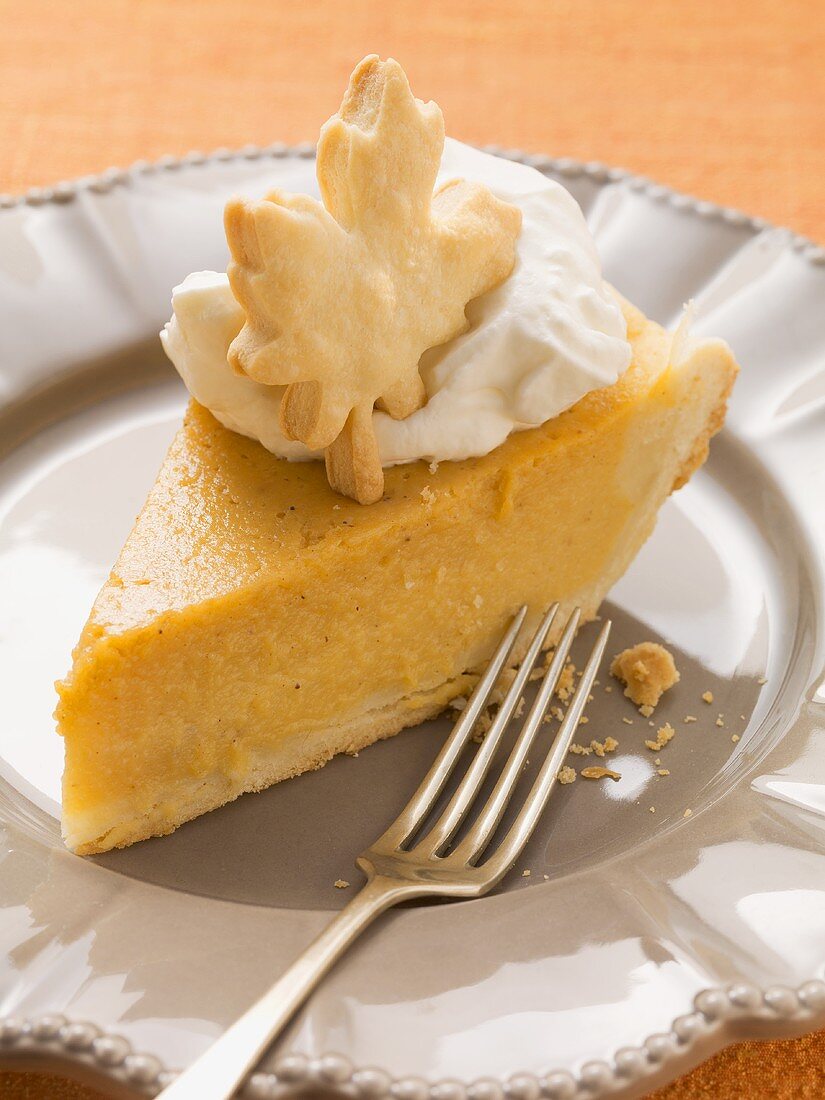 Piece of pumpkin pie with cream and pastry leaf