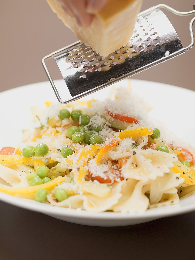 Hand grating Parmesan onto farfalle with vegetables