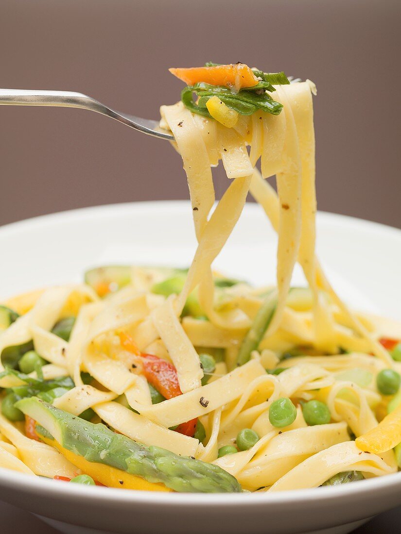 Ribbon pasta with vegetables on fork and plate