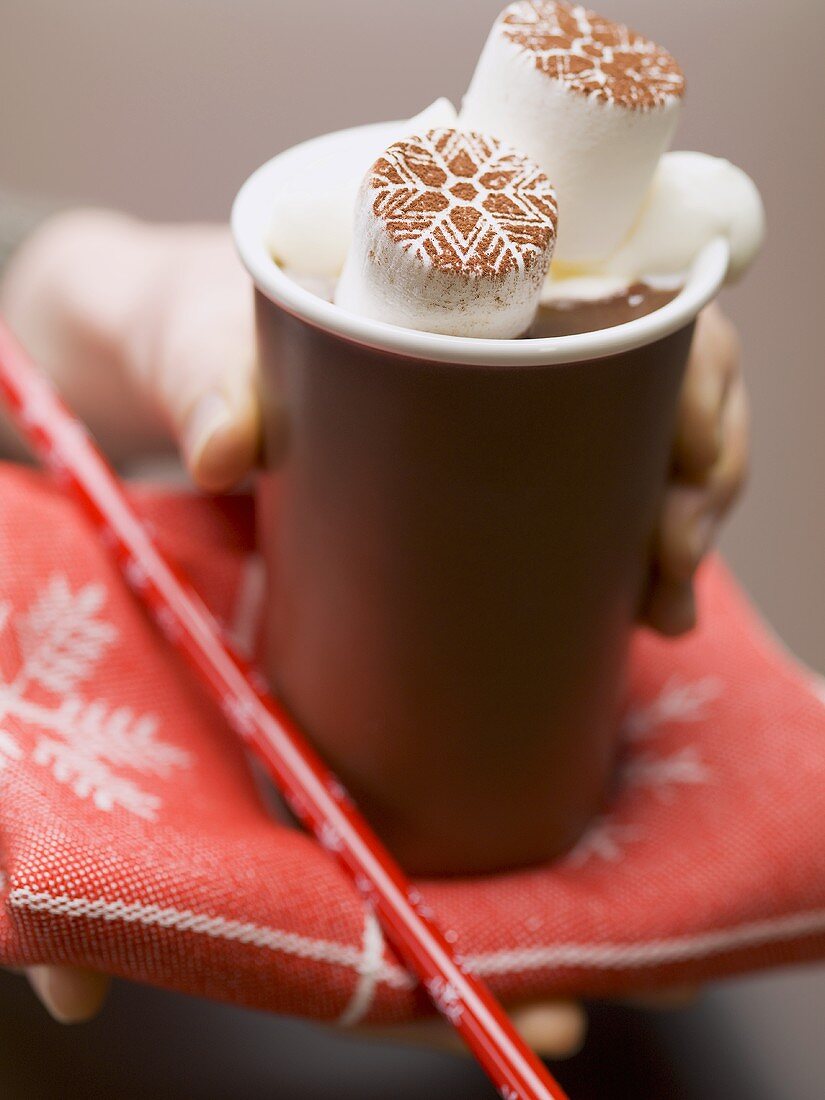 Hand holding beaker of hot chocolate with marshmallows & cream