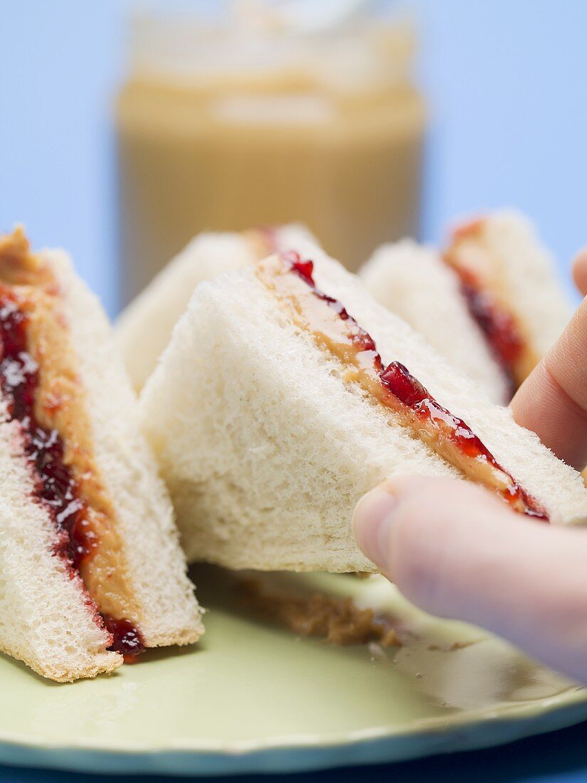 Hand reaching for peanut butter and jelly sandwich
