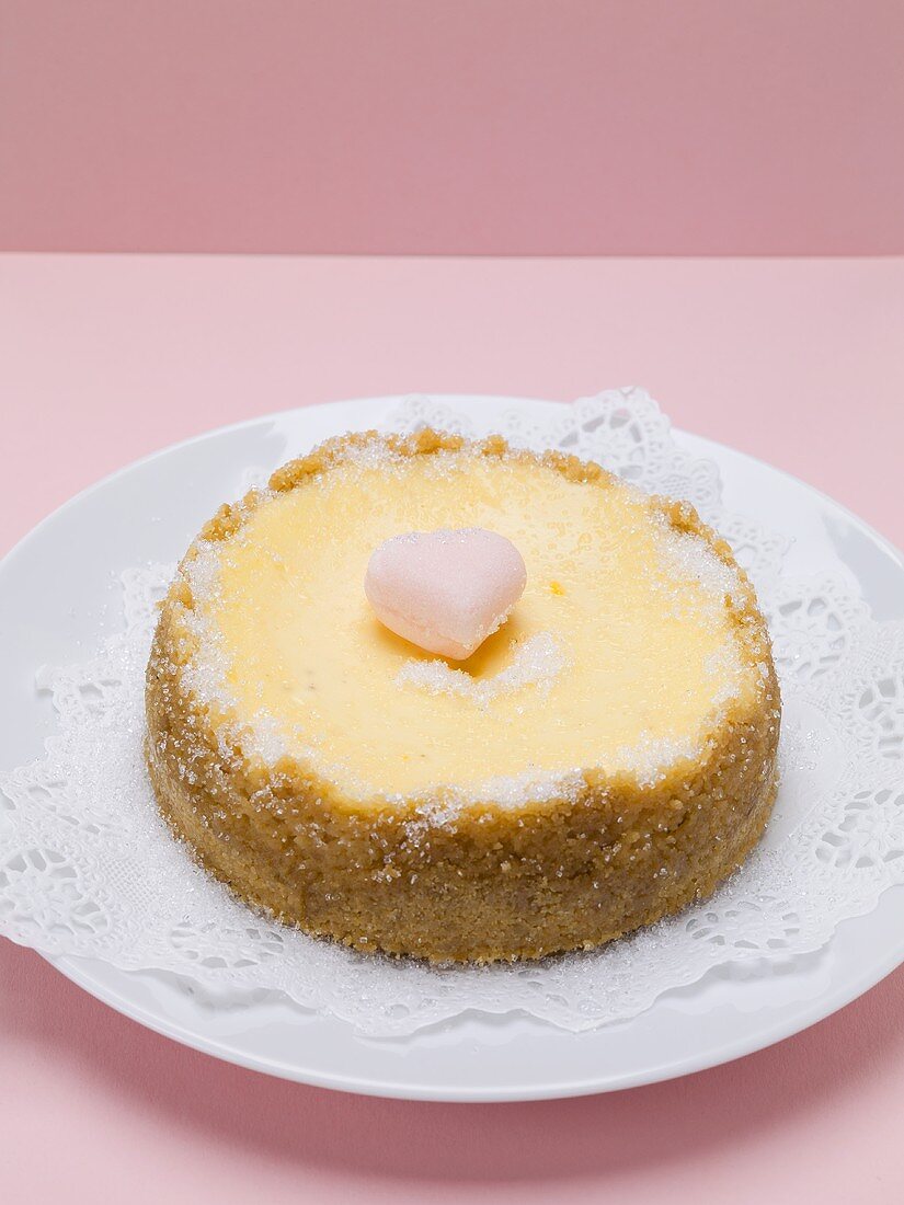 Small cheesecake with sugar heart on plate with doily