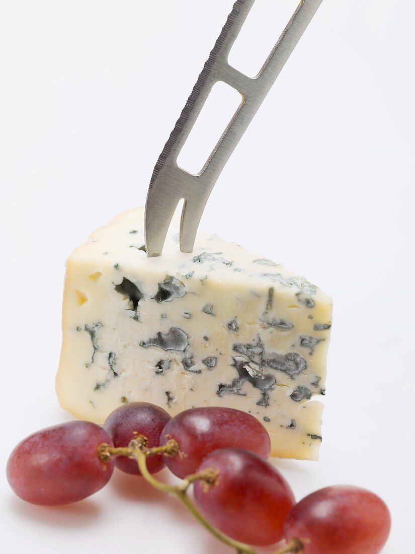Stück Blauschimmelkäse mit Käsemesser und roten Trauben