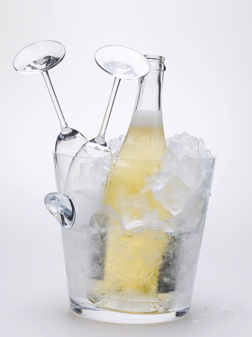 Bottle of sparkling wine & two empty wine glasses in ice bucket