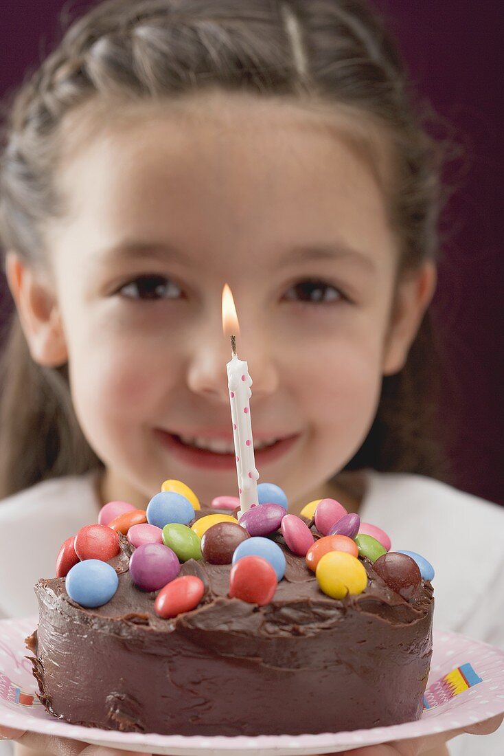 Mädchen hält Geburtstagstorte mit Schokolinsen und Kerze