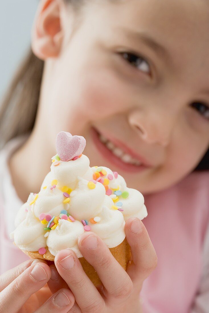 Kleines Mädchen hält Cupcake mit Sahne und Zuckerkonfetti