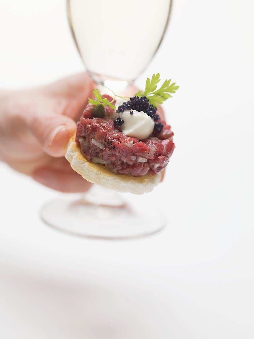 Hand holding sparkling wine glass and tuna tartare canapé