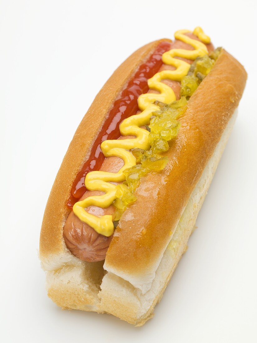 A hot dog with ketchup, mustard and gherkin