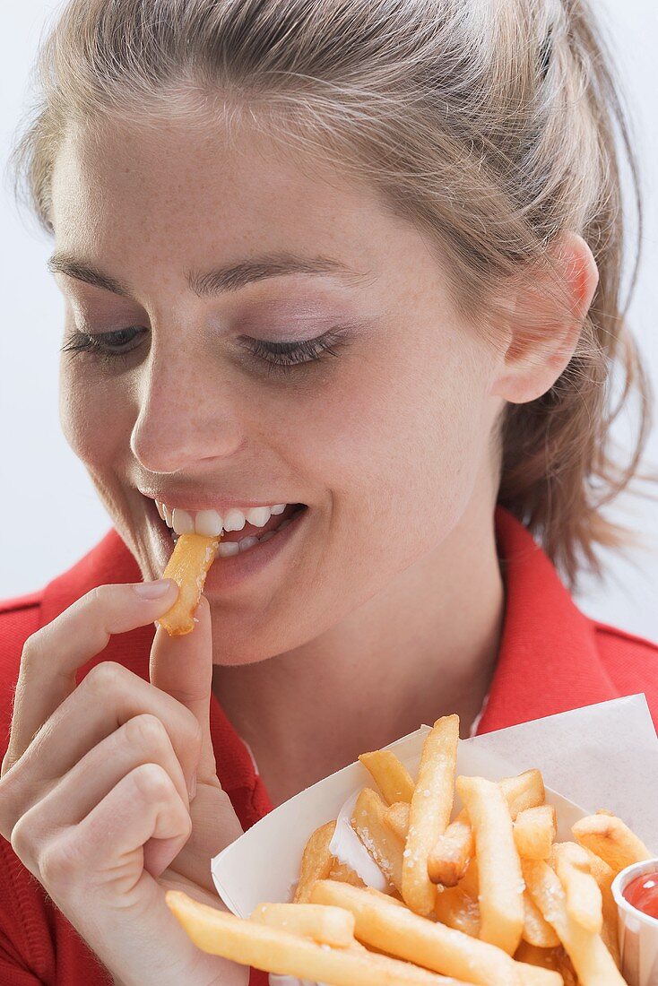 Junge Frau mit Pommes Frites- Tüte beim essen