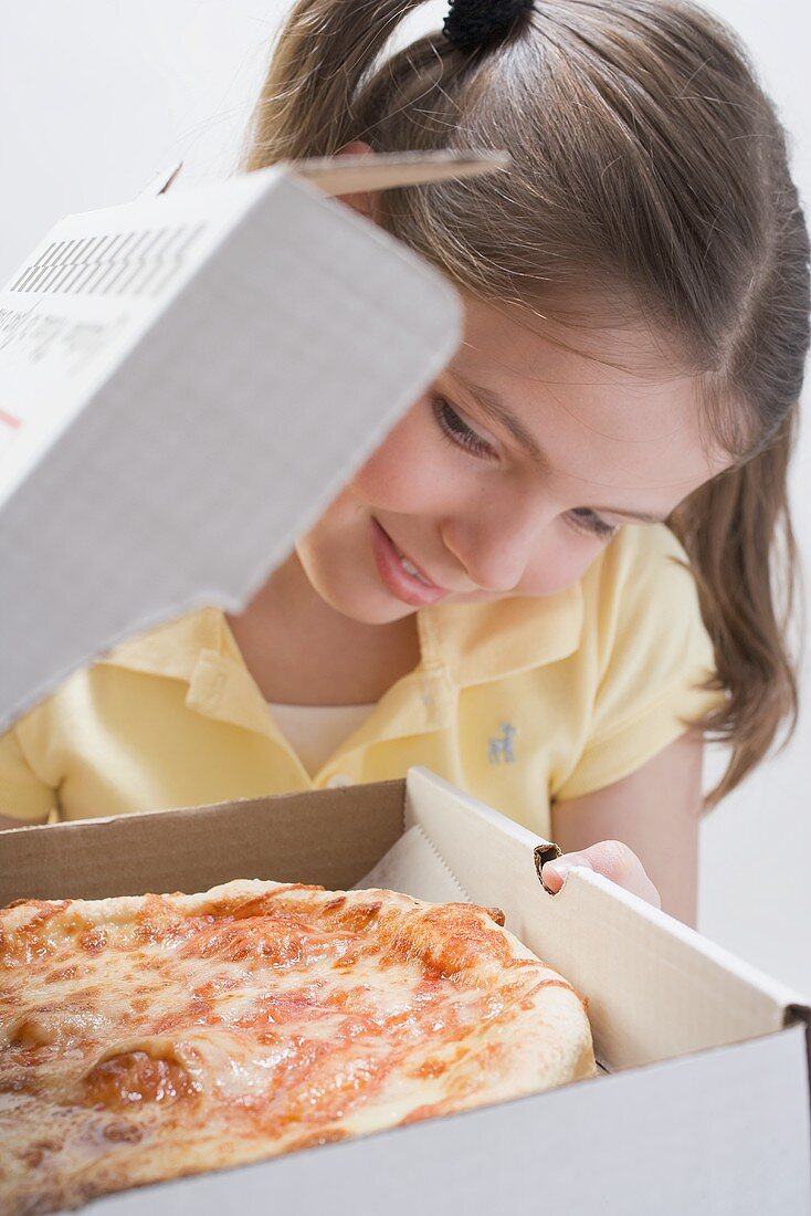 Mädchen schaut in Pizza-Schachtel mit frischer Pizza