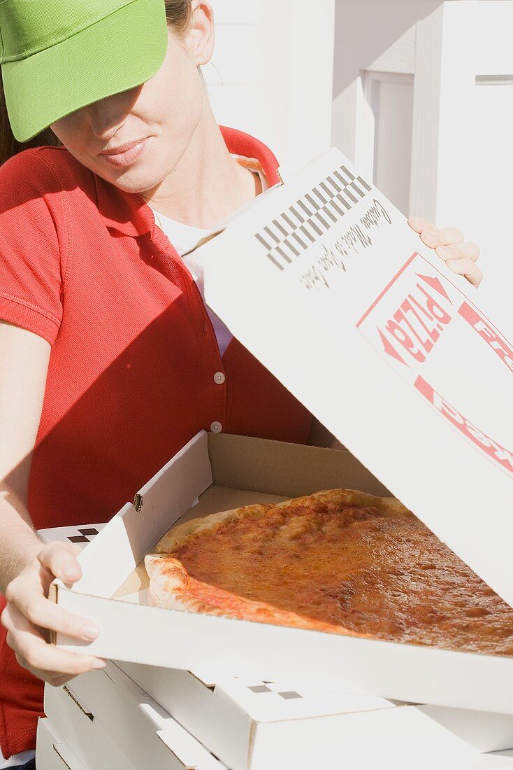 Frau mit Schirmmütze schaut in die geöffnete Pizzaschachtel