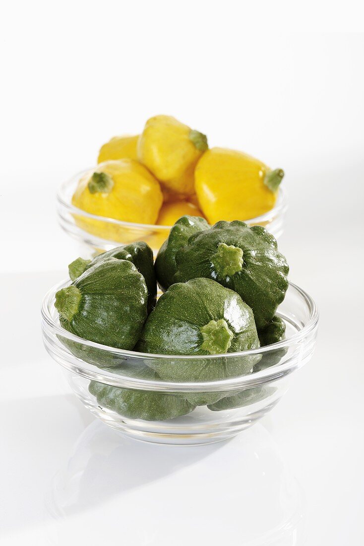 Green and yellow patty pan squashes in glass bowls