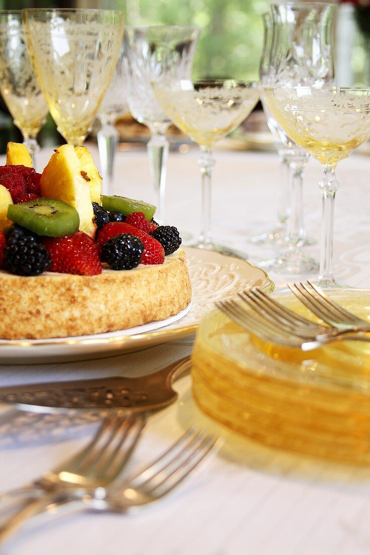 Fruit Tart on Table with Stacked Plates and Stem Glasses
