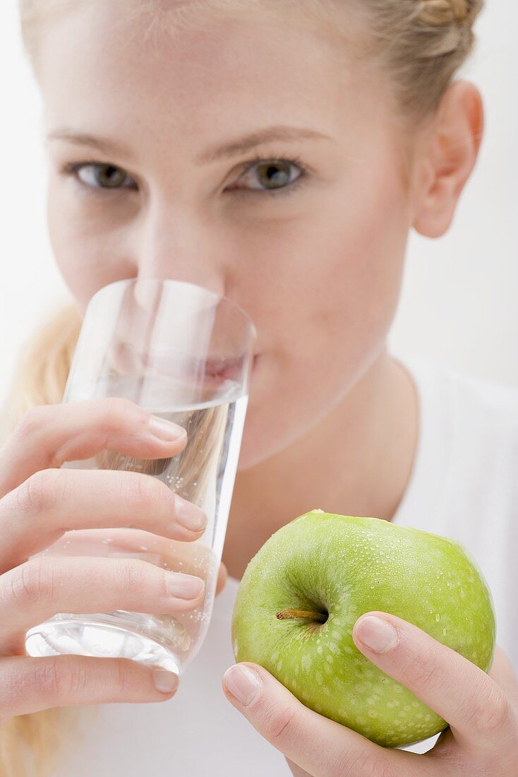 Frau hält Apfel und trinkt Glas Wasser