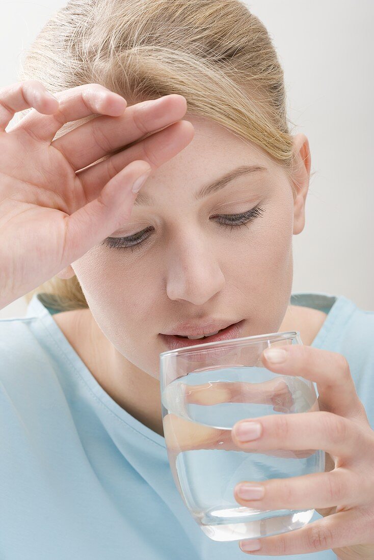 Woman with headache drinking glass of water