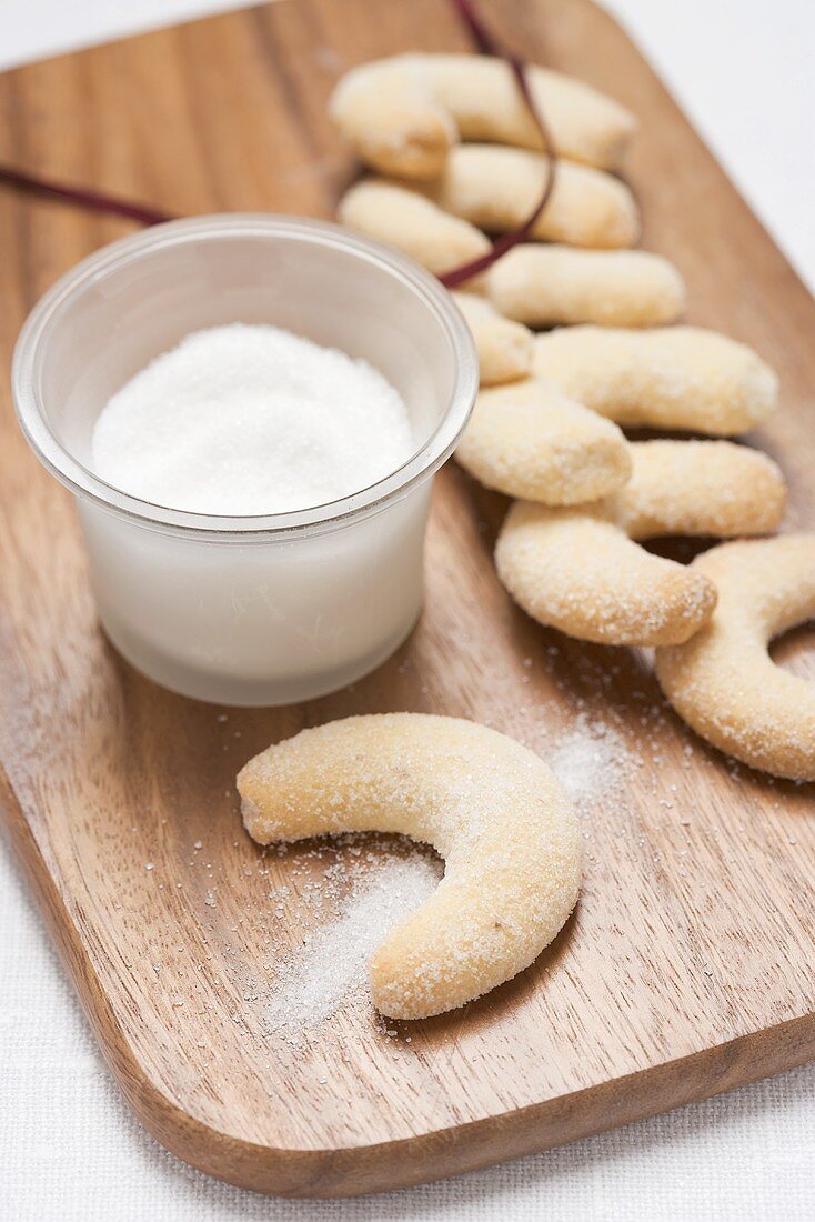 Vanilla crescents and a glass of sugar on chopping board