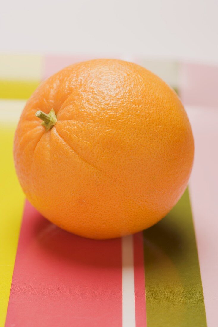 Eine Orange auf gestreiftem Stoffuntergrund