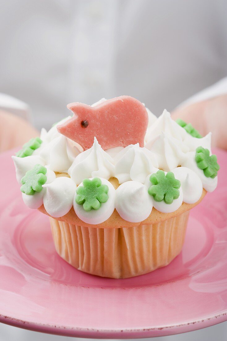 Hands holding cupcake with marzipan pig on pink plate