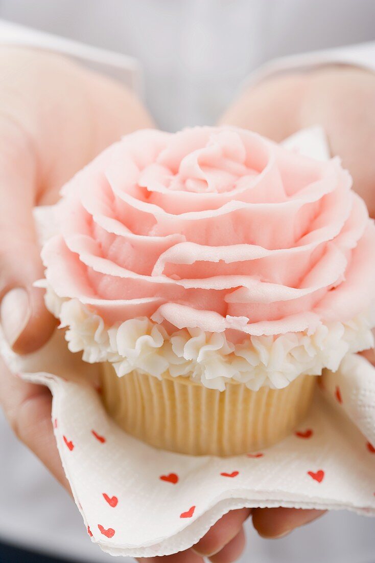 Hands holding cupcake with marzipan rose