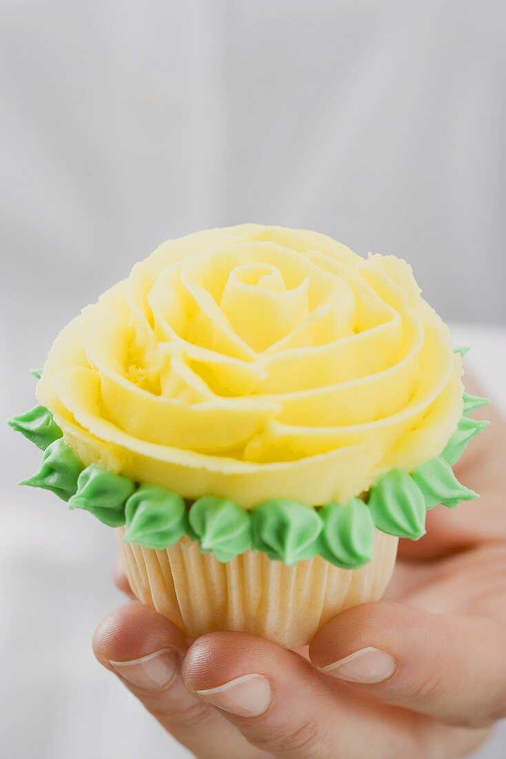 Hand hält Cupcake mit gelber Marzipanrose