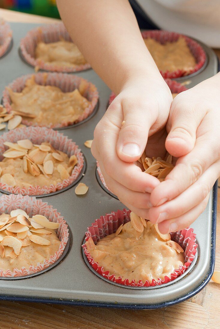 Child sprinkling flaked almonds on unbaked muffins