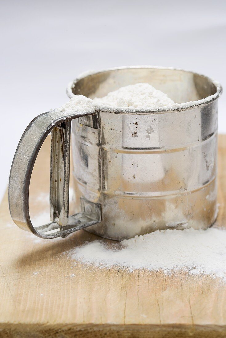Flour in flour sifter on chopping board