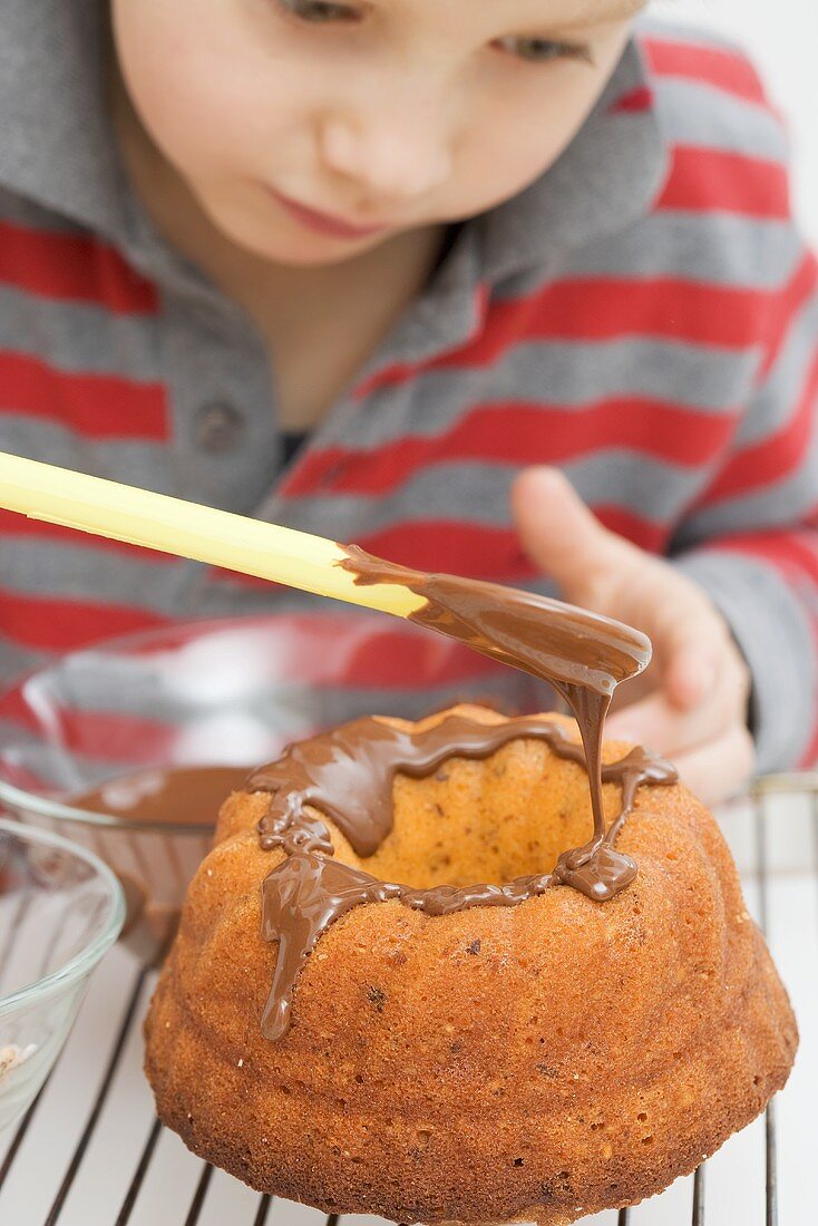 Kleiner Junge verziert Napfkuchen mit Schokoglasur