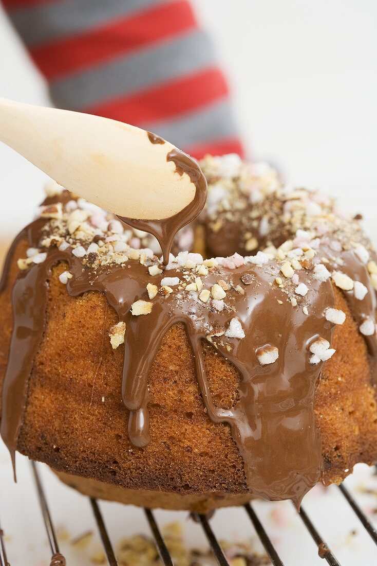 Child decorating ring cake with chocolate icing and chopped nuts