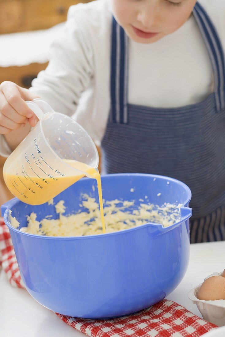 Little boy pouring egg yolk into butter mixture