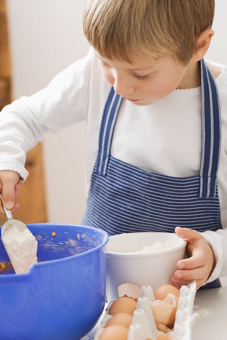Little boy putting flour into mixing bowl
