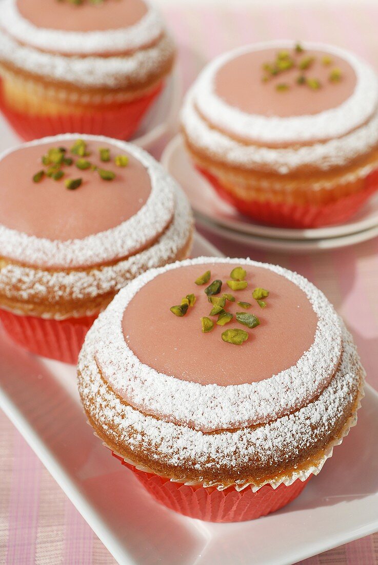 Four pink marzipan muffins with icing sugar and pistachios